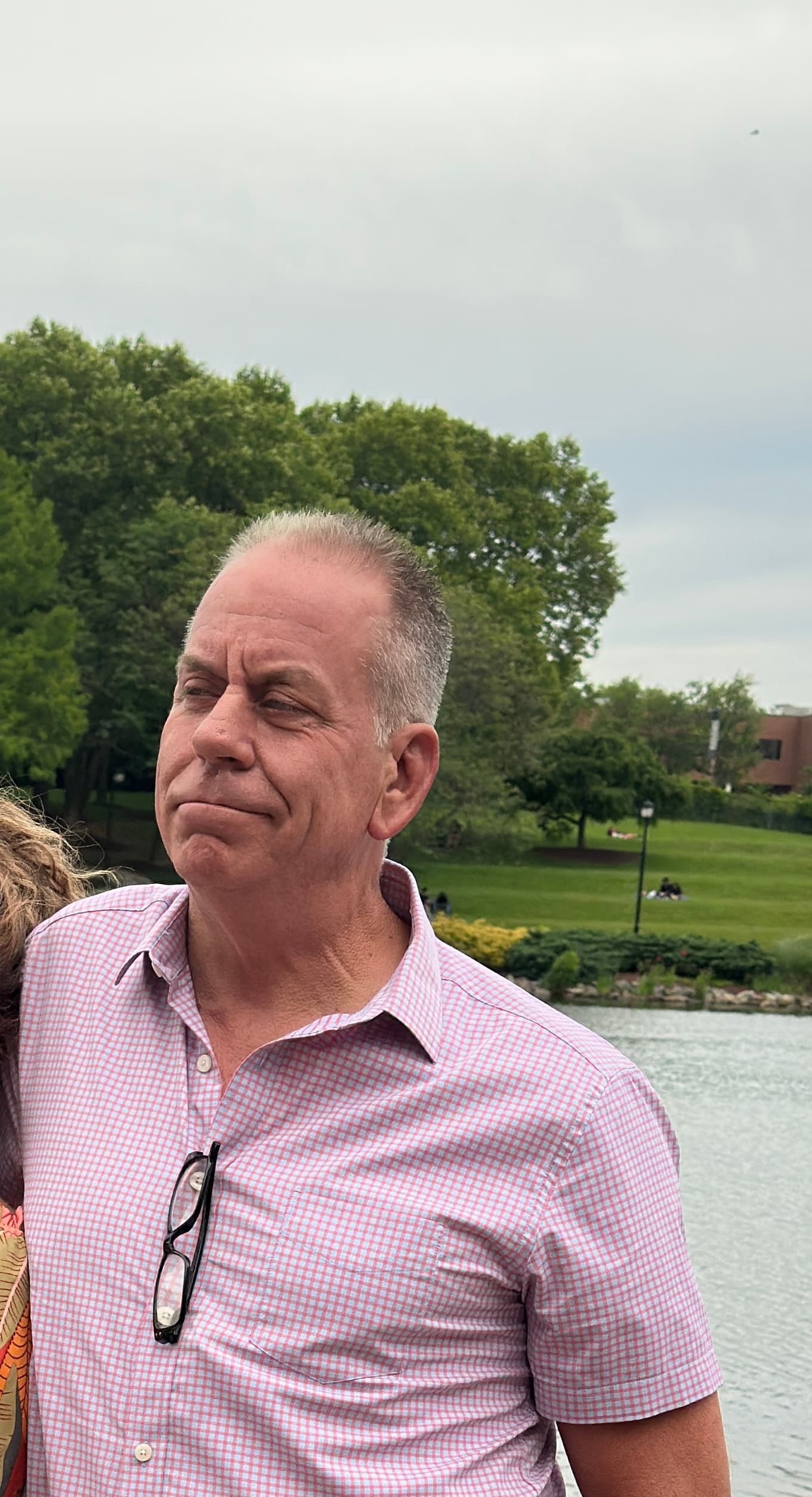 Middle-aged man in a pink checkered shirt looking aside near a park and lake.